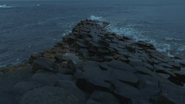 Slow motion shot of ripples splashing on Gian's Causeway basalt hexagonal columns. Blue hour, cinematic.
