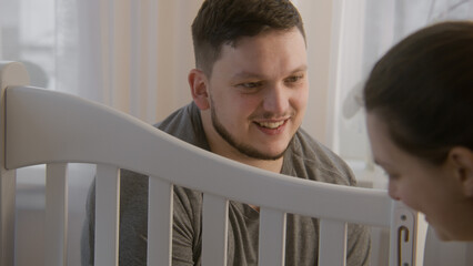 Close up view couple looking at each other and assembling crib for newborn baby at nursery. Loving...