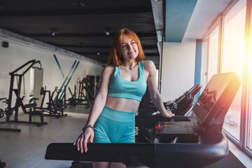 young skinny sporty female athletic stand near  treadmill trainers and rest after exercise at gym