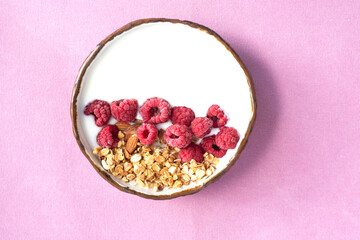 Healthy and tasty breakfast - yogurt bowl with raspberry, cereals and nuts pink cloth background