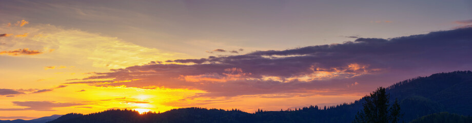 sky panorama at dusk. glowing clouds above the mountain silhouette in evening light