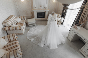 Fototapeta na wymiar an exquisite wedding dress with a long train on a mannequin is located in a hotel room with a royal interior. Wide angle