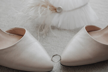 The wedding ring is held by the tips of the shoes, behind the garter is decorated with feathers, on a gray background