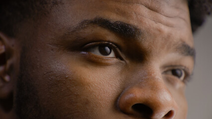 Detailed portrait of young African American man straight and serious face with confident look. Concentrated guy looks away, blinks eyes, poses on camera. Man stands in studio on the grey background. © Framestock