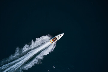Large high speed white boat with orange chairs and people fast moving on dark water top view.