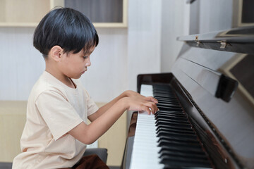 Kid asian black hair boy sitting and playing piano in living room house indoor. Musical and relaxation makes them happiness. Health care lifestyle concept.