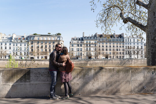Heterosexual couple kissing with beautiful parisian buildings on the background during their vacations in Paris.