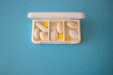 different capsules lie in a white open pill box on a blue background. View from above - 591758532