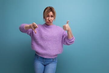 distressed upset blond young woman in purple hoodie showing like and dislike on blue background...