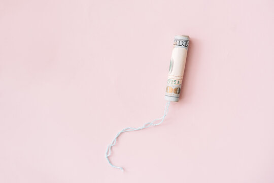 Tampon wrapped in a dollar bill on a pink background.