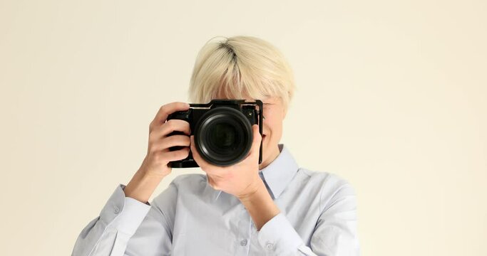 Young woman with dyed blonde hair takes photos with professional camera. Skilled photographer points modern device to camera smiling slow motion