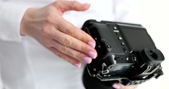 Woman puts memory card into professional camera closing cap. Photographer sets up modern device ready to make photos in studio slow motion