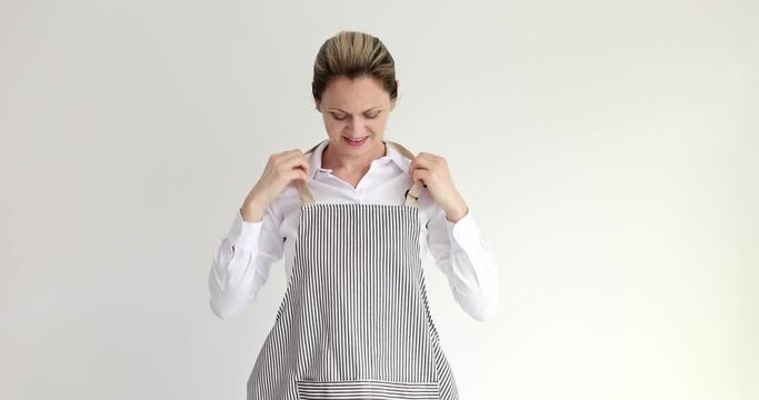Happy woman puts on striped apron looking in camera and smiling on beige background. Female maid ready for cleaning hotel rooms slow motion