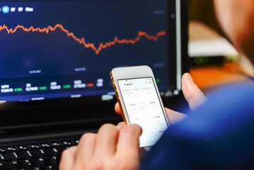 Trade and finance concept.Businessman checking stock market by his smartphone and laptop.Caucasian Male using mobile phone investing application.Stock market investment and trading app in hand.