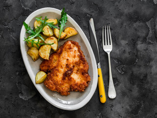 Chicken milanese with crispy potatoes and rocket salad jy the dark background top view