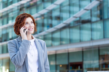 Young executive woman smiling on phone with glass building in background and looking at copy space