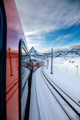 A red train in pov perspective driving along a snowy landscape, in the distance you can see the matterhorn