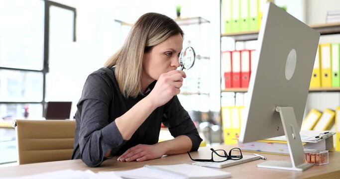 Suspicious woman looks at screen of computer through magnifier glass. Female employee tries to read small font on website slow motion