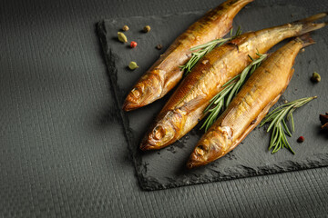 Smoked capelin fish on a serving board with rosemary served for lunch. Dark space for menu or prescription.