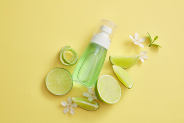 Flat lay of a transparent pump bottle filled with green liquid extracted from Lime (Citrus aurantiifolia), decorated with flowers and Lime slices. Natural cosmetic products. Unbranded mock-up