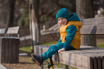 A little boy walks in the spring on the playground. A child is sitting on a bench in the fresh air on a sunny spring day. Childhood and child development.