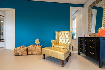 A gold-colored armchair in a waiting room with tables, a chest of drawers and a mirror next to it - 591777171