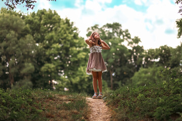 Happy childhood. Cute little schoolgirl girl in a straw hat and dress standing on a slope and looks...