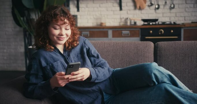 African Asian woman relaxes scrolling social media on sofa
