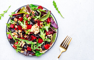 Beet and herbs healthy salad with prunes, arugula, chard and walnuts, gray table. Fresh useful vegan dish for healthy eating