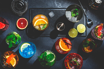 Cocktails set on black bar counter, top view. Mixology concept. Assortment of colorful strong and low alcohol drinks for cocktail party. Dark background, bar tools, hard light - obrazy, fototapety, plakaty