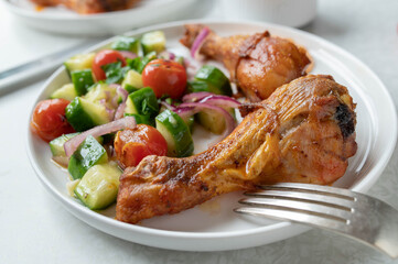 Oven baked chicken drumsticks with cucumber tomato salad on a plate