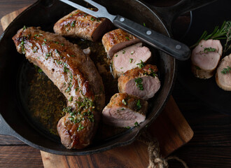 Pan fried pork fillet in melted herb butter in a cast iron pan on wooden table from above