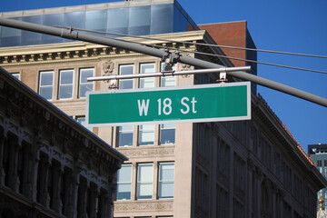 Green big West 18th Street sign hanging on a arch pole in the streets of midtown Manhattan