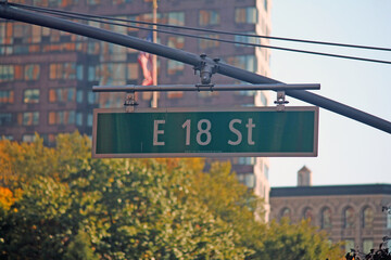 Green big East 18th Street sign hanging on a arch pole in the streets of midtown Manhattan