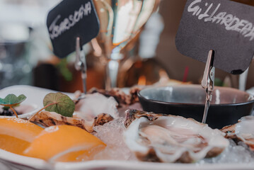 Fototapeta premium Fresh Oysters close up on a plate, served table with oysters, lemon and ice. Healthy sea food. Fresh Oyster dinner with sparkling wine in a restaurant. Gourmet food