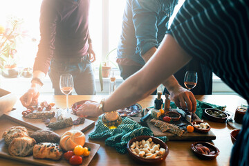 View of the hands of different people reaching out to take tapas food arranged on the table during a tasting