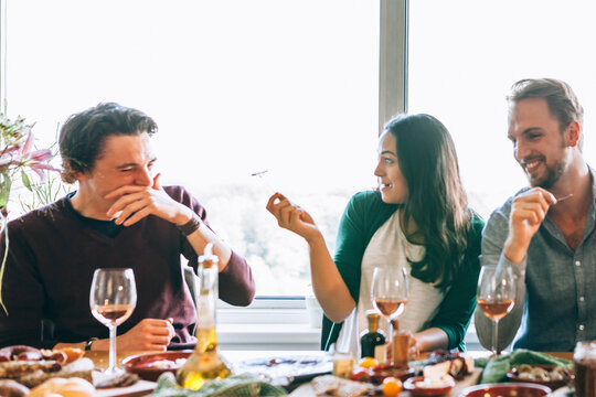 Friends laugh and joke, making remarks to each other while sitting at the table during a festive lunch