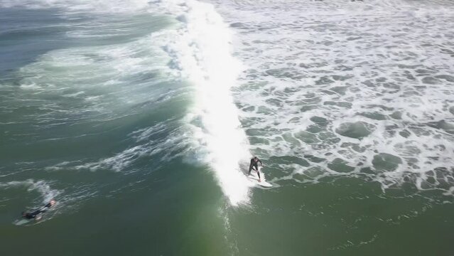 Drone shot of surfer catching waves at famous Coxos surf spot in Ericeira, Portugal. Aerial view showcases natural beauty and raw power of ocean. Highlights popularity as top surfing destination.