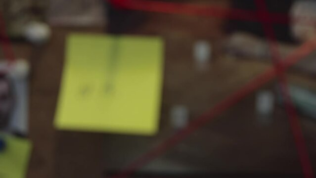 The camera slowly zooms out to reveal a board with evidence, photos, documents, all connected by a red string