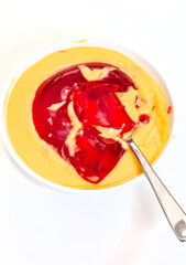 Bowl of red jelly and custard and spoon on white