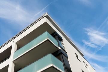 Corner of a residential building with balconies against a blue sky with light clouds. Bottom view.