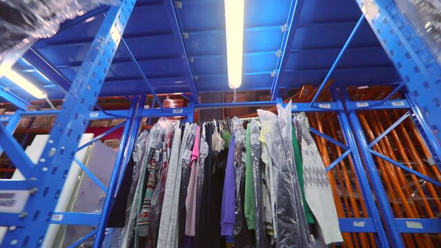 The clothes are hung in rows in the warehouse. Warehouse with clothes. Clothes in the warehouse of the factory. industrial interior