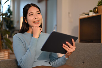 Smiling adult woman sitting on couch browsing wireless internet on digital tablet. Technology, people and lifestyle concept