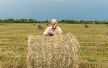Naklejka na ściany i meble A man sitting on a large armful of straw in an empty field. Against the blue sky.