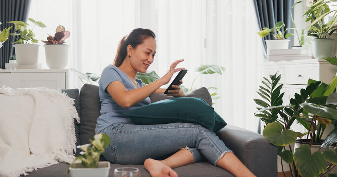 Young Asian woman wear casual site on couch use smartphone feel exciting scrolling screen online shopping in living room indoor plants at home. Excited and surprised female holding cellphone concept.