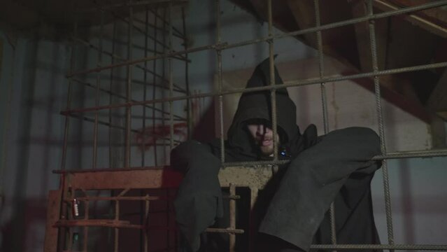 Man behind prison bars. The executioner person in jail. Halloween or horror movie concept. High quality FullHD footage with slow motion