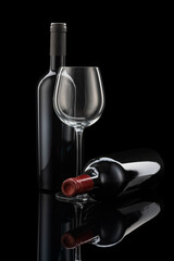 2 wine bottles, one standing and one lying and a wine glass in front of a black background
