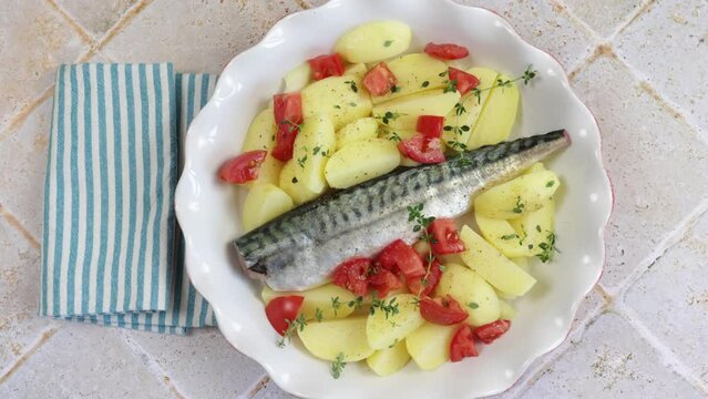 poisson (maquereau) avec pommes de terre, tomate, thym et oignons dans un plat	