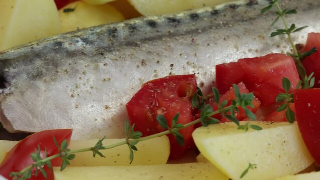 poisson (maquereau) avec pommes de terre, tomate, thym et oignons dans un plat	