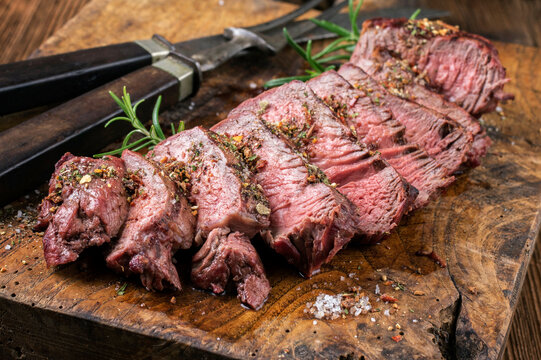 Barbecue dry aged entrecote beef steak sliced and served as close-up on a rustic wooden board